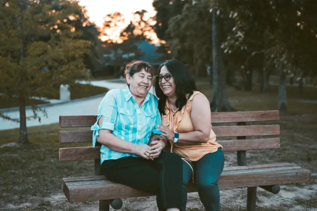 two middle-aged hispanic women embracing self-discovery, sharing a close moment on a park bench, laughing