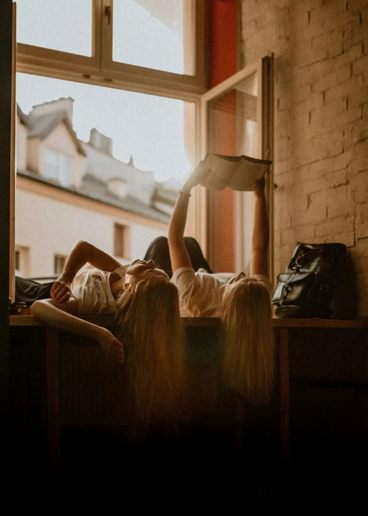 two women deepening intimacy, spending quality time together reading a book near an open window