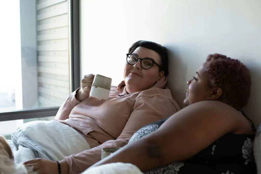 Plus-size lesbian couple drinking morning coffee in bed